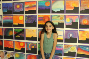 student posing in front of a wall of artwork